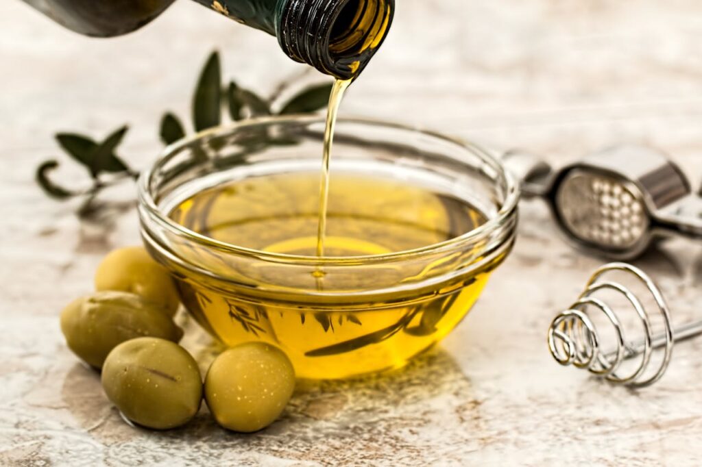 olive-oil-salad-dressing-cooking-olive Close-up of olive oil being poured into a glass bowl surrounded by fresh olives and kitchen tools.